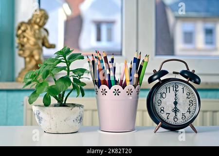 Alarm clock next to Colorful pencils and potted plant on table. Back to school and home office concept. Stock Photo