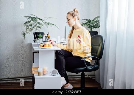 Freelancer young woman eating healthy food when working from home. Woman eating Healthy Grain Snacks and fruits while working with laptop at home Stock Photo