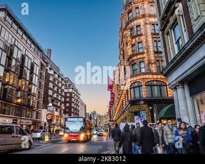 BROMPTON ROAD KNIGHTSBRIDGE WINTER SALES with red bus and Harrods department store behind at dusk night with lit 'Sale' sign busy shoppers crowds traffic sunset Harrods Knightsbridge London SW1 Stock Photo