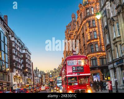 BROMPTON ROAD HARRODS KNIGHTSBRIDGE WINTER SALES with vintage retro red routemaster private travel tour bus and Harrods department store behind at dusk, night with lit 'Sale' sign busy shoppers traffic Harrods Knightsbridge London SW1 Stock Photo