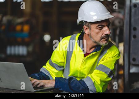 professional technician engineer with safety hard hat working to maintenance construction equipment in industrial factory, inspection man having manuf Stock Photo