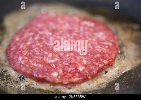 Closeup of a fresh meat burger frying in the frying pan with a small focus. Beef burger. Stock Photo