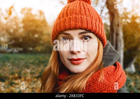 Autumn fashion portrait of stylish woman in bright orange knitted hat and scarf. Red hair, big black eyes, bright lipstick. Walk in sunny park with ye Stock Photo