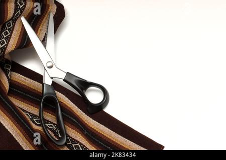 Thick brown patterned fabric and sewing scissors  isolated on white background. Stock Photo