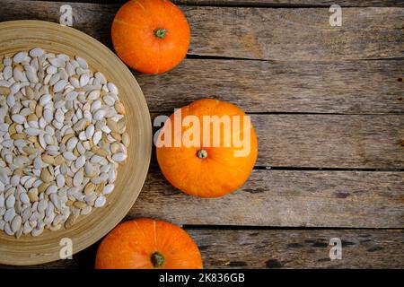 Pumpkins and pumpkin seeds in plate on wooden background Stock Photo