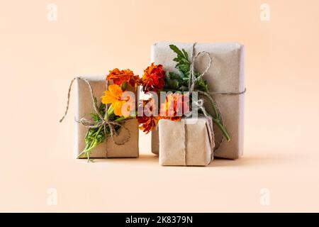 Gift box in gray craft paper decorated with orange flowers marigolds on an orange background for the holiday, flat lay Stock Photo