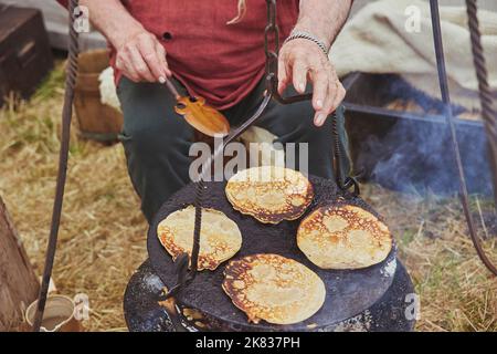 Old man frying pancakes in a pan on a campfire Stock Photo