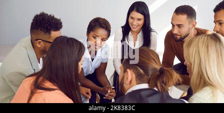 Group of happy young diverse people sitting in a circle and having a conversation Stock Photo