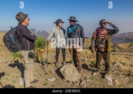 SIMIEN MOUNTAINS, ETHIOPIA - MARCH 17, 2019: Tourists, local tour guide and an armed scout guarding tourists in Simien mountains, Ethiopia Stock Photo