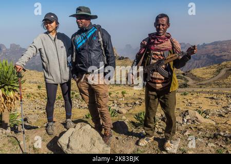 SIMIEN MOUNTAINS, ETHIOPIA - MARCH 17, 2019: Tourist, local tour guide and an armed scout guarding tourists in Simien mountains, Ethiopia Stock Photo