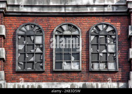 brick facade of an abandoned building with broken windows, an old uninhabited house in a dilapidated state, a deserted city, nobody. Stock Photo