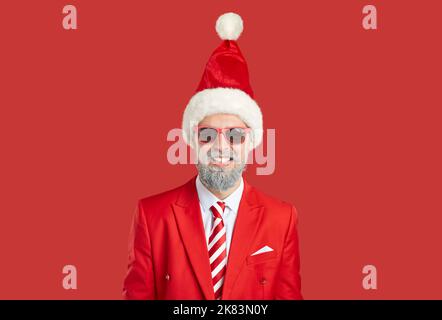 Portrait of happy bearded man wearing red suit, sunglasses and funny Christmas hat Stock Photo