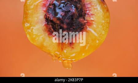 cut peach with juice dripping on an orange background Stock Photo