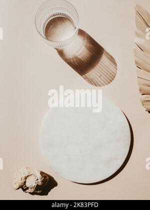 Marble white round podium, water glass. palm leaf and texture stone on beige background. Place, Flat lay. background . Top view. Copy space Stock Photo