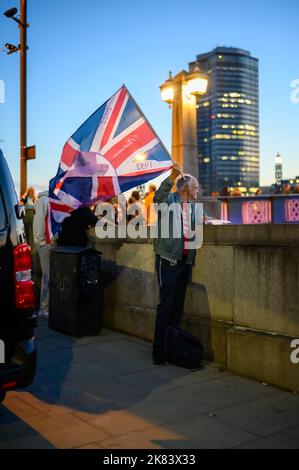London - September 17, 2022: Man waves Union Jack flag with Queen's face on it. Early evening light of setting sun Stock Photo