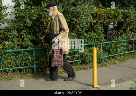 Old man is walking down street. Pensioner on track. Old man in yard. Man with bag and stick. Grey hair. Stock Photo