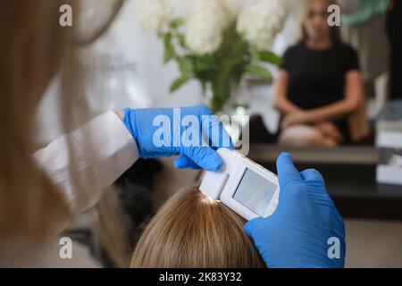 Doctor examines head skin of young woman with special dermatology equipment system, hairloss and trichology concept. Analyzing Hair With Analysis Stock Photo