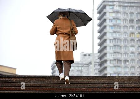 Woman with umbrella walking up the steps on buildings background. Rain in autumn city Stock Photo