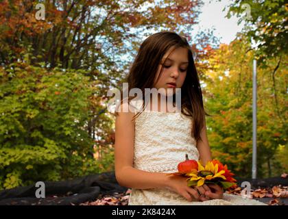 Beautiful young girl sitting on a trampoline holding sunflowers and a small pumpkin in Autumn Stock Photo