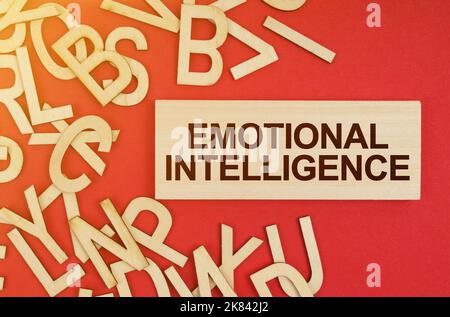 Business and finance concept. On a red background, there are wooden letters and a plate with the inscription - Emotional Intelligence Stock Photo