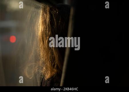 Girl sits by glass on bus. Hair for girl by window. Inside bus. Passenger in transport. Man in front on seat. Stock Photo