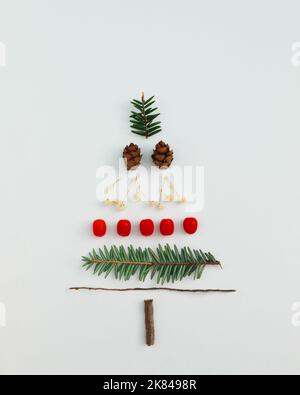 Christmas tree made with evergreen fir, pine cones, red berries and branches on white background. Minimal holiday flat lay composition. Winter creativ Stock Photo