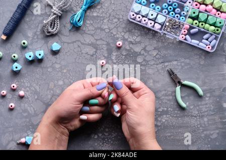 Handmade jewelry. Box with beads, hands with tools. Making handmade jewelry for yourself or as self made custom gifts. Flat lay on grey textured Stock Photo
