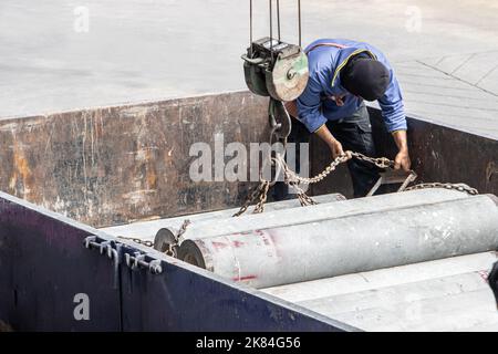 A worker attaches chains from a crane to concrete tubes on the load space of a truck Stock Photo