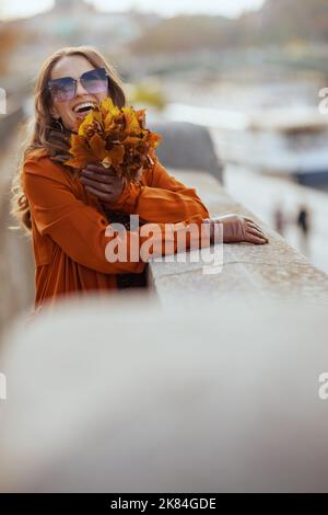 Hello autumn. smiling stylish woman in brown trench coat with autumn yellow leaves in the city. Stock Photo