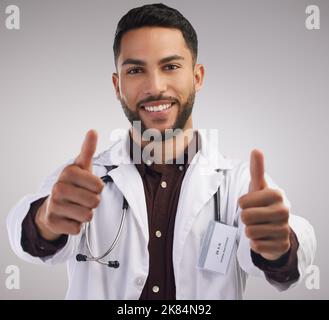 Youre in good hands. a handsome young doctor standing alone in the studio and making a thumbs up hand gesture. Stock Photo