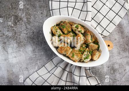 Fried pollock fish in a white baking dish on a dark grey background. Top view, flat lay Stock Photo