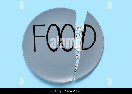 Cracked plate with word FOOD and measuring tape on color background. Anorexia concept Stock Photo