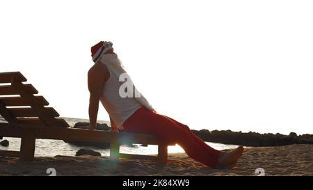 funny santa claus sunbathes. santa lies on wooden lounger on beach by the sea, relaxing, at sunrise. santa claus is on summer vacation, at the seashore. High quality photo Stock Photo