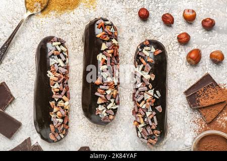 Tasty chocolate eclairs and hazelnuts on light background, closeup Stock Photo