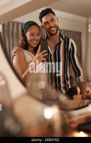 Selfie with my love. a young couple standing together and using a cellphone to take mirror selfies during a dinner party. Stock Photo