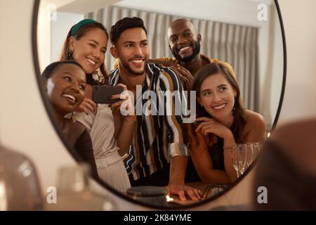 May we continue creating epic memories together. a young group of friends using a cellphone to take mirror selfies during a New Years dinner party. Stock Photo