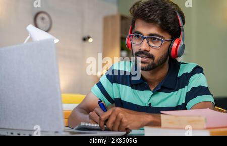 studnet writing notes by seeing laptop at home - concept of online education, remote learning and intelligence. Stock Photo