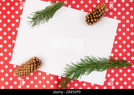 Fir twigs and cones on red background with polka dot and white sheet for text. Christmas, New Year, autumn, winter. Copy space Stock Photo