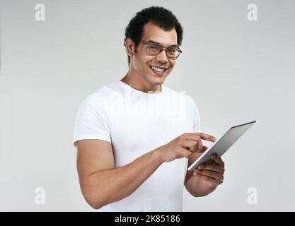 Let me show you what this app can do. a man using a digital tablet while standing against a grey background. Stock Photo