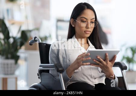 Using the tools at her disposal. an attractive young businesswoman in a wheelchair using her tablet in the office. Stock Photo