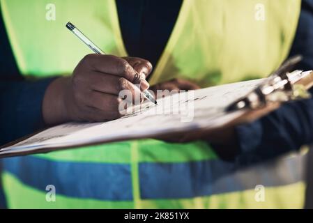 Signing off the shipment. an unrecognizable contractor standing alone in the warehouse and writing on a document during stock-take. Stock Photo