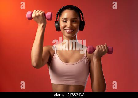 Keep going, dont give up. Studio portrait of a sporty young woman exercising with dumbbells against a red background. Stock Photo