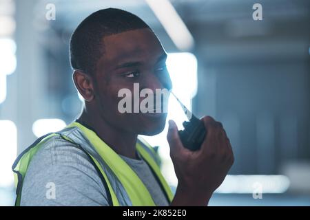 Can you bring the forklift please. a handsome young contractor standing alone in the warehouse and using a walkie talkie. Stock Photo
