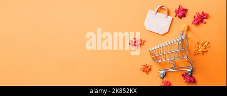 Autumn shopping design concept with shopping cart and maple leaves on orange table background. Stock Photo