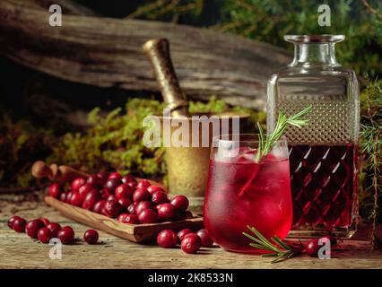 Cranberry cocktail with ice and rosemary in frozen glass. In the background moss, juniper branch, and old snag. Stock Photo