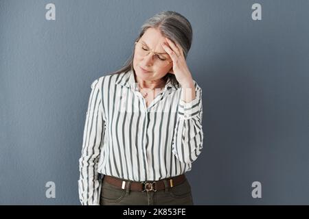 Your ancestors have already fought your battles, youre okay. a mature businesswoman holding her head suffering an intense headache against a black Stock Photo
