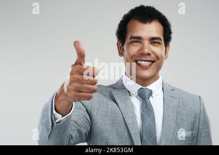 Business is going good. Studio shot of a confident businessman showing thumbs up while standing against a grey background. Stock Photo