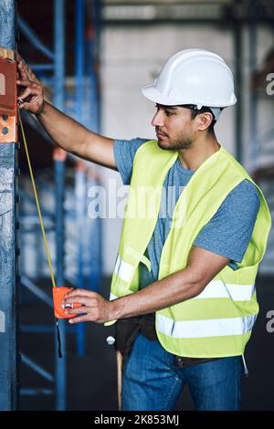 Leave no room for error. a young builder using a measuring tape at a construction site. Stock Photo