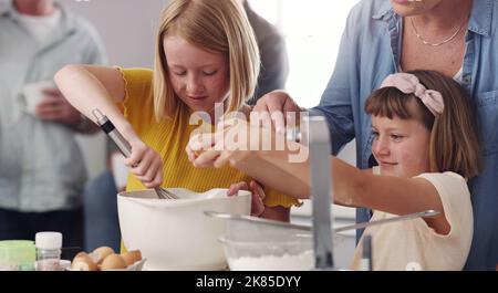 Getting out hands dirty with flour. two little girls baking with the assistance of their mother. Stock Photo