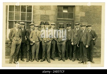 Original 1920's era postcard, sepia tinted in places, of office staff, group of working class men standing outside their office, lots of characters, wearing suits and assortment of hats - flat caps, bowler and Homburg hats. Just before the Great Depression started in 1929. Dated April 1928, U.K. Stock Photo